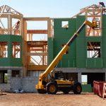 A multi-story wooden house under construction using a crane on a sunny day.