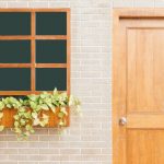 A wooden door and window on a light brick wall adorned with green leafy plants.